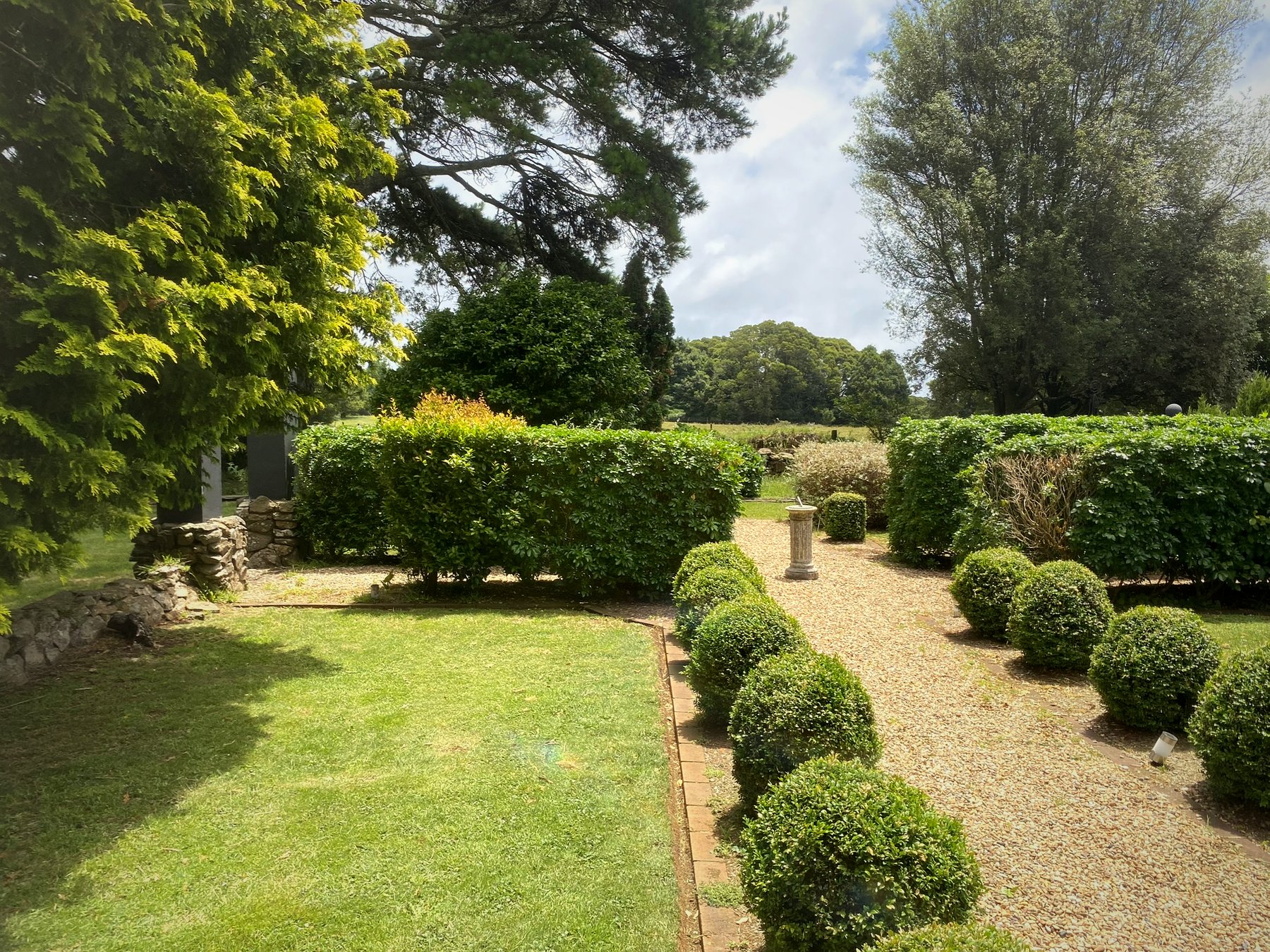 Formal garden with topiary box hedging, gravel pathways, stone sundial and manicured lawn surrounded by mature trees at Lemmons Rd Robertson