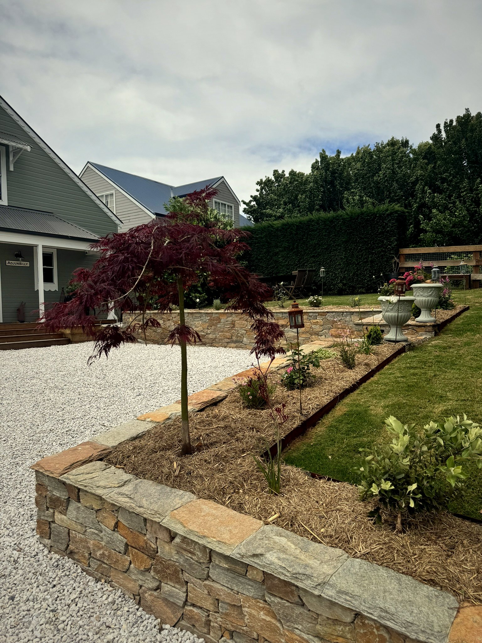 Landscaping project with stone retaining walls, Japanese maple, mulched garden beds, white gravel driveway and steel edging at Main St Robertson